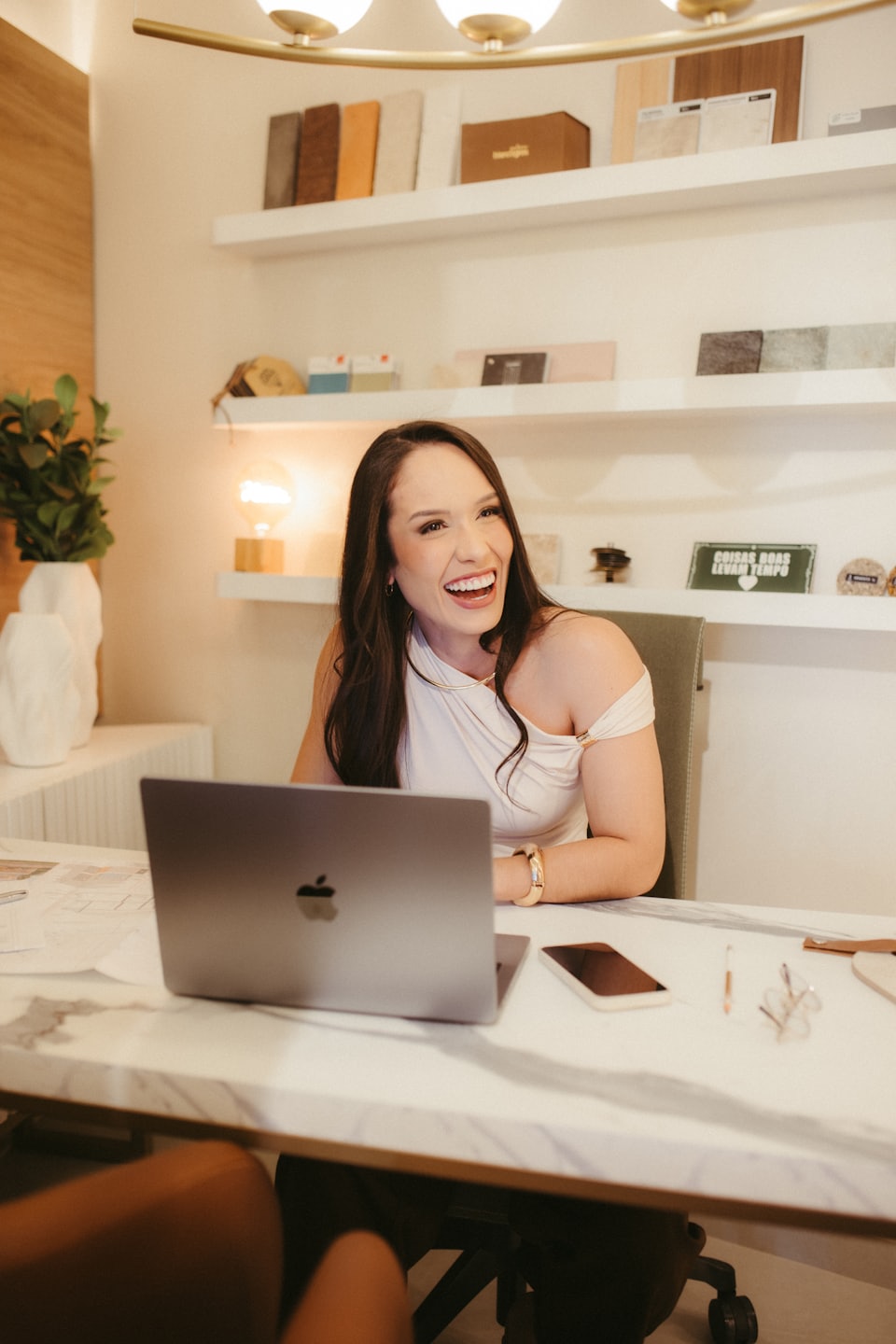 Woman smiles while working on a laptop at a marble desk.