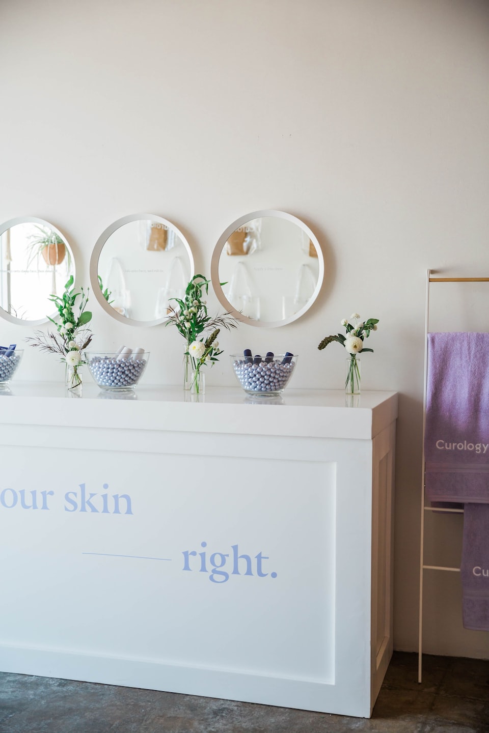 Skincare samples on a counter with floral arrangements and lavender towels.